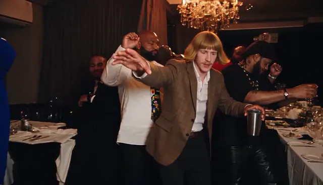 Burning Bridges AI video opening: the lead walks into the chandelier party room holding a silver cup